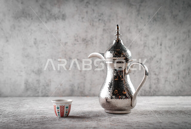 Arabic coffee pot, close-up of a glass cup next to the jug, enjoyment in serving hot drinks, traditional hospitality in the Kingdom of Saudi Arabia, the quality of local national products, a gray background