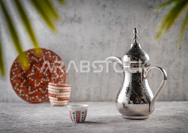 دله قهوة عربية, إكرام الضيف وحسن الاستقبال,صورة مقربه لإبريق نحاسي مع فنجان القهوة, العادات العربية القديمة في تقديم القهوة, جودة المنتجات المحلية الوطنية, تقديم المشروبات الساخنة, السلال اليدويه المنسوجه التراثية, خلفية رماديه
