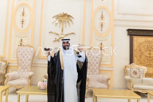 معرس شاب سعودي خليجي بتعابير وجه تدل على السعادة ،  يرقصو يحمل بيده السيف ، عريس بالزي السعودي الرسمي ، مناسبات الزواج