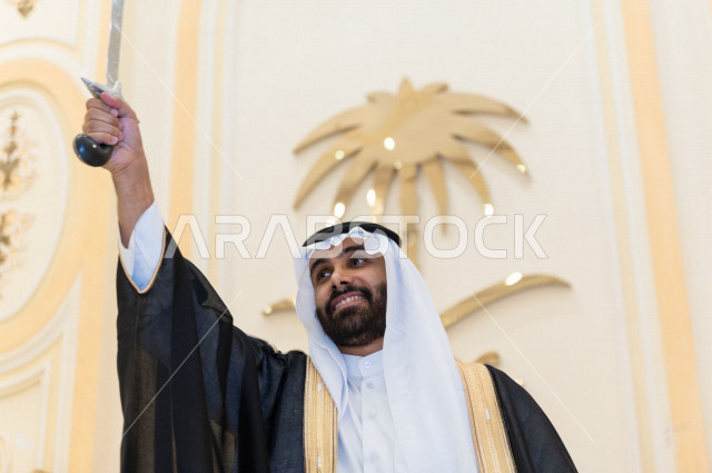 معرس شاب سعودي خليجي بتعابير وجه تدل على السعادة ،  يرقصو يحمل بيده السيف ، عريس بالزي السعودي الرسمي ، مناسبات الزواج