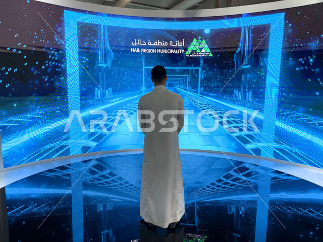 الفرص الاستثمارية للمشاريع العقارية في معرض سيتي سكيب العالمي، صورة من الخلف لشاب عربي خليجي سعودي يقف امام شاشة هولوجرامية رقمية تفاعلية ثلاثية الابعاد في جناح منطقة حائل، مركز الرياض للمعارض في بلدة ملهم في السعودية، الاستدامة والتخطيط المعماري لقطاع العقارات