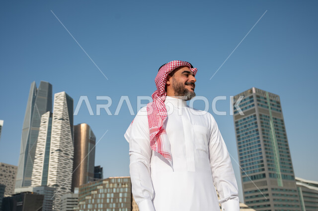 النمو والتطور العمراني في السعودية، رجل عربي خليجي سعودي يرتدي الشماغ والثوب التقليدي بإيماءات وجه تدل على السعادة والفرح، الفن الهندسي المعماري للأبراج وناطحات السحاب في الرياض، المباني المالية والمنشآت الإقتصادية، خلفية مركز الملك عبد الله المالي (كافد) 