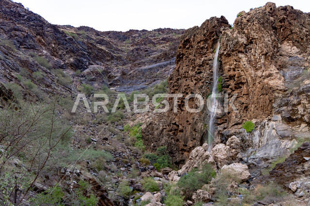 Prominent historical archaeological landmarks in the Kingdom of Saudi Arabia, tourist entertainment places, a natural waterfall between the mountainous and rocky peaks and heights in the Asir region, nature background.