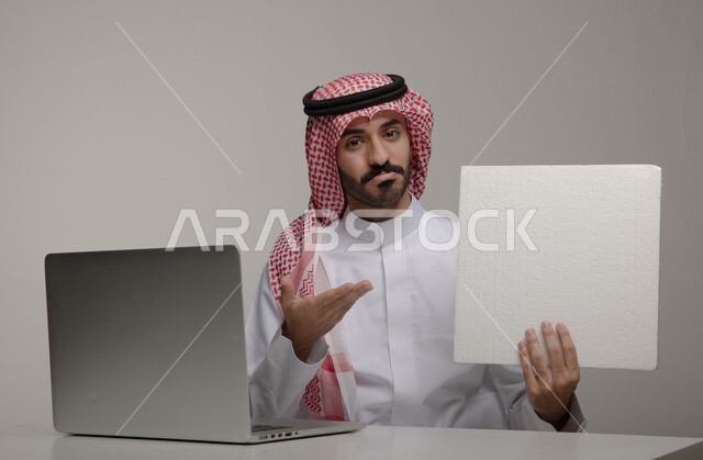 الفشل في إنجاز المهام بإتقان ،الإشارة إلى الورقة بإيماءات وجه تدل على الحزن والخسارة , بورتريه لرجل عربي خليجي  سعودي يرتدي الزي التقليدي ويحمل بيده ورقة بيضاء فارغة , تصفح الإنترنت والعمل عن بعد من خلال اللابتوب ، استخدام الحاسوب المحمول في المكاتب ، خلفية رمادية