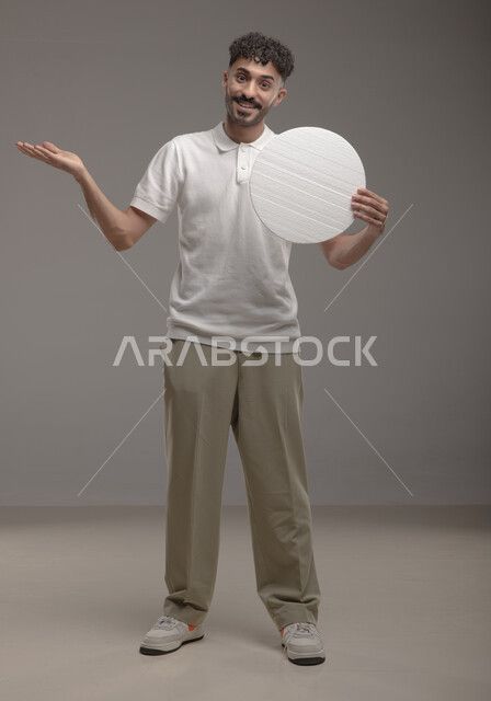 عرض لوحه بيضاء دائريه، النظر الى الكاميرا بإيماءات السرور و الرضا، موك اب دائري أبيض، بورتريه لرجل عربي خليجي سعودي مبتسم مسرور يرتدي الزي الكاجوال و يحمل بيده لوح إعلاني فارغ، الوقوف باستقامه وثقه، صورة الجسم بالطول الكامل، خلفية رماديه