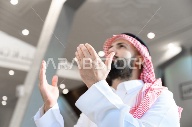 A Saudi Muslim man inside the mosque, raises his hands up and prays to God, beseech God and ask for forgiveness, worship and draw close to God