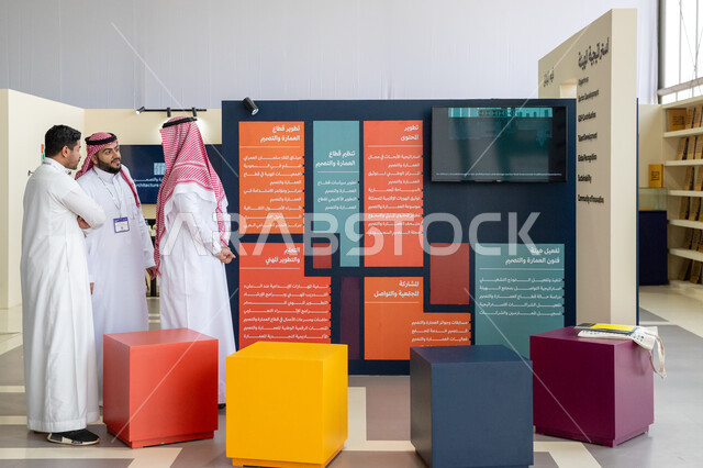 لوحات ومخططات المشاريع في إحدى الاجنحة في معرض سيتي سكيب العالمي، مجموعة رجال عرب خليجيون سعوديون يرتدون الزي التقليدي يتناقشون بالفرص الاستثمارية في المشاريع السكنية والتجارية، رؤية مستقبلية 2030، مركز الرياض للمعارض في بلدة ملهم في السعودية، الاستدامة والتخطيط المعماري لقطاع العقارات