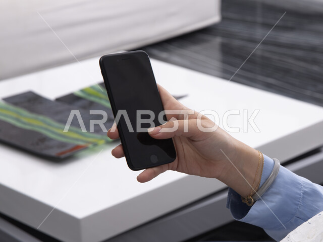 استخدام حاسة اللمس بالتقنيات الحديثة ,إمرأة عربية خليجية سعودية  تحمل بيدها جهاز الهاتف المحمول ، ايماءات يدين بالنقر بالاصبع على الشاشة ، تصفح الانترنت والتسوق الالكتروني  , إجراء مكالمة هاتفية , البحث عن عمل .