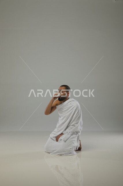 الارتواء والشرب من ماء زمزم ، الدعاء والعباده والتقرب الى الله، بورتريه جانبي لرجل مسلم عربي سعودي خليجي يرتدي ملابس الاحرام ويجلس على ركبتيه، آداء فريضة الحج، موسم العمرة في شهر رمضان المبارك،  خلفية رمادية
