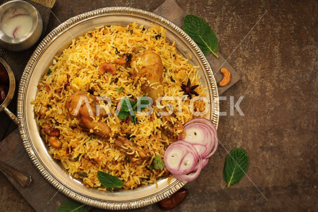 الأرز البخاري  المطهي بالبهارات الطبيعية  الطازجة ,صورة من الأعلى لطبق من كبسة الدجاج المزين بشرائح البصل والبقدونس ,  وصفات طعام شهية , مطابخ ومطاعم سعودية شرقية , خلفية بنية 