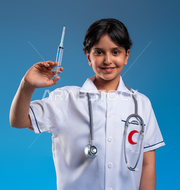 أمنيات و آمال مستقبيله في العمل في المختبرات والتحاليل ،مفهوم الطب والرعاية الصحية، بورتريه مقرب لفتاة  عربية خليجية سعودية مبتسمة ترتدي زي الطبيب وتحمل بيده حقنة طبية، ايماءات الحب و الشغف بالحصول على الشهادات العليا، خلفية زرقاء