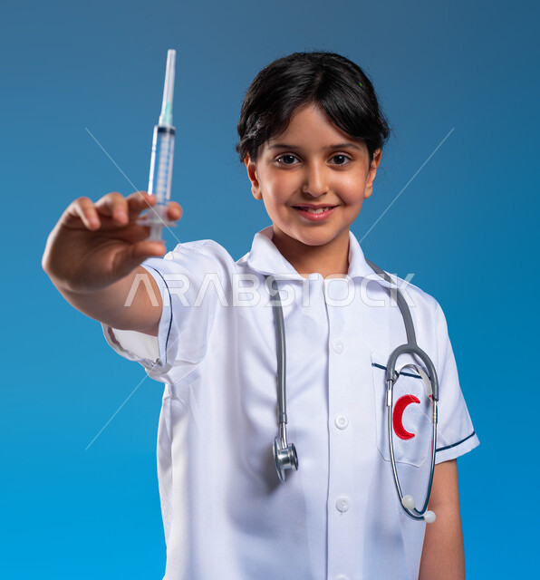 آمال وأمنيات مستقبيله في العمل في المختبرات والتحاليل ،مفهوم الطب والرعاية الصحية، بورتريه مقرب لفتاة  عربية خليجية سعودية مبتسمة ترتدي زي الطبيب وتحمل بيده حقنة طبية، ايماءات الحب و الشغف بالحصول على الشهادات العليا، خلفية زرقاء