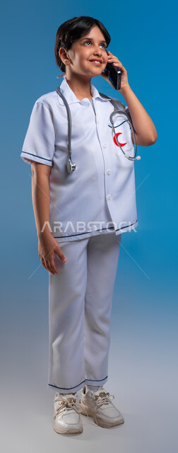استخدام التكنولوجيا للإستشارات الطبية ،بورتريه لفتاه عربية خليجية سعودية مبتسمة ترتدي زي الطبيب تقوم بإجراء مكالمة هاتفيه عبر الجوال تحلم ان تصبح طبيبة اسعافات أولية، تلبية مطالب الرعاية الصحية عن بعد باستخدام التقنيات الحديثة، صورة الجسم بالطول الكامل، خلفية زرقاء