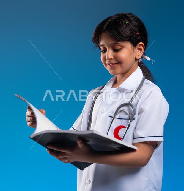 مراجعة المواعيد و تنظيم الوقت، الطموحات و الأهداف المستقبلية في العمل في العيادات والمشافي ،بورتريه مقرب لفتاة عربية خليجية سعودية مبتسمة ترتدي اللباس الابيض الخاص بمهنة الطب و تنظر إلى الملفات الخاصة بالمرضى، تحديد واختيار مهنة المستقبل منذ الصغر، خلفية زرقاء
