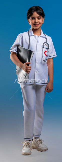 التأهب بأن تصبح طبيبة إسعاف وطوارئ، الطموحات و الأهداف المستقبلية في العمل في العيادات والمشافي ،بورتريه لفتاة عربية خليجية سعودية مبتسمة ترتدي اللباس الابيض الخاص بمهنة الطب وسماعة الطبيب تحمل بيدها ملفات المرضى الخاصة، صورة الجسم بالطول الكامل، خلفية زرقاء