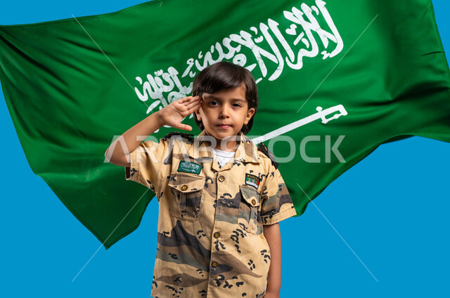 يوم العلم السعودي ١١ مارس، الاحتفال باليوم الوطني ٢٣ سبتمبر،  القوات المسلحة السعودية، حب الدفاع عن الوطن، الوقوف باستعداد وانضباط، ولد عربي سعودي خليجي يرتدي الزي العسكري ويقوم بإلقاء التحية العسكرية متمنياً أن يصبح جندي، صورة الجسم بالطول الكامل، خلفية زرقاء