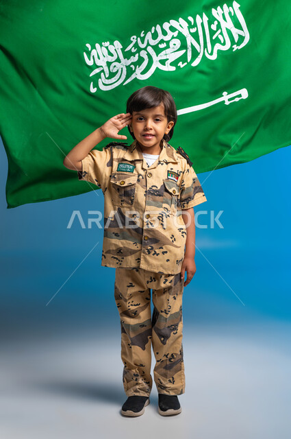 الاحتفال باليوم الوطني ٢٣ سبتمبر، يوم العلم السعودي ١١ مارس، القوات المسلحة السعودية، حب الدفاع عن الوطن، الوقوف باستعداد وانضباط، ولد عربي سعودي خليجي يرتدي الزي العسكري ويقوم بإلقاء التحية العسكرية متمنياً أن يصبح جندي، صورة الجسم بالطول الكامل، خلفية زرقاء