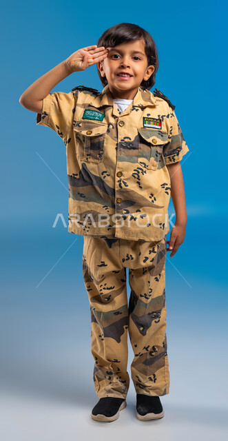 القوات المسلحة السعودية، الدفاع عن الوطن، الوقوف باستعداد وانضباط، بورتريه  لولد عربي سعودي خليجي يرتدي الزي العسكري ويقوم بإلقاء التحية العسكرية متمنياً أن يصبح جندي ،  صورة الجسم بالطول الكامل، خلفية زرقاء