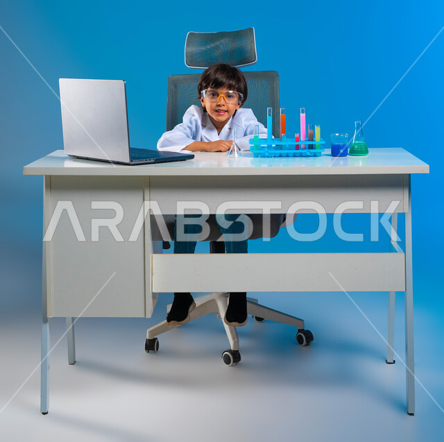 امنيات المستقبل كطبيب مختبرات كيميائيه,  بورتريه لولد عربي سعودي خليجي مبتسم يرتدي معطف أبيض و يضع نظارات واقية لإجراء التفاعلات الحيوية، استخدام أنابيب الأختبار، تدوين النتائج المخبرية على جهاز الحاسوب، استخدام انابيب الاختبار الزجاجيه، خلفية زرقاء