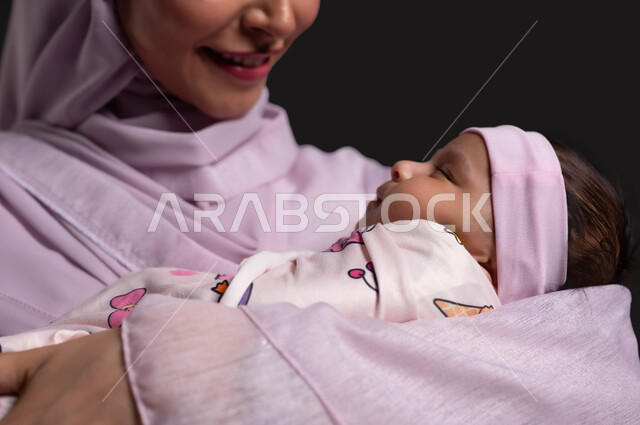 تقديم الدعم العاطفي للطفل الرضيع، استمداد الرضيع الطمأنينة والاستقرار من الأم، بورتريه مقرب لإمرأة عربية خليجية سعودية محجبة ترتدي العباءة وتنظر الى طفلتها بحب وحنان، مفهوم الأمومة والطفولة،  خلفية سوداء