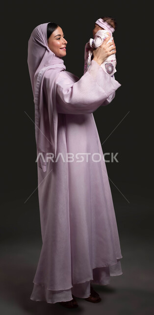 Sacrifice and dedication for the happiness and comfort of the child, maternal affection and care for children, the role of the mother towards her children, spending quality time with the children, close-up portrait of a veiled Saudi Arabian Gulf woman wearing an abaya and enjoying playing with her daughter, full-length body portrait, black background