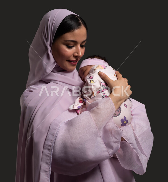 إيماءات الاسترخاء والأمان، التعامل مع الاطفال الرضع، بورتريه مقرب لسيدة عربية خليجية سعودية محجبة ترتدي العباءة وتضم ابنتها الى صدرها بحب وحنان، الحاجة للراحة والنوم، مفهوم الامومة والطفولة، خلفية سوداء