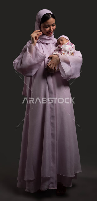 Strengthening the relationship of trust and affection between mother and child, trying to wake the child from sleep, portrait of a veiled Saudi Arabian Gulf woman wearing an abaya and moving her fingers in gestures of playing with her daughter, the concept of motherhood and childhood, full-length body image, black background