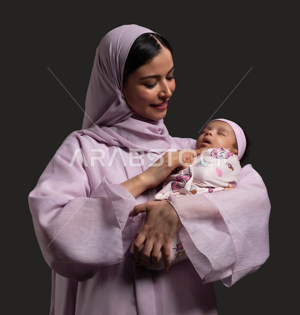 تقوية رابط المحبة بين الأم وأطفالها، بورتريه مقرب لأم عربية خليجية سعودية محجبة ترتدي العباءة الملونة وتنظر الى رضيعتها بحب وحنان، اللعب مع البنات برفق وعطف، الحاجة للراحة والنوم، خلفية سوداء