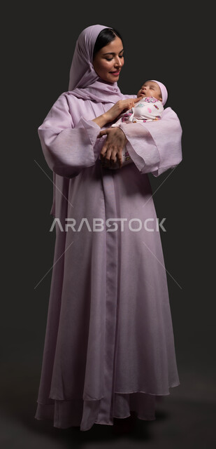Mothers’ sacrifice and dedication for their children, a portrait of a veiled Saudi Arabian Gulf mother wearing a colorful abaya and contemplating her infant daughter with love and tenderness, strengthening the relationship of trust and affection between mother and child, feeling of comfort and security, full-body portrait, black background