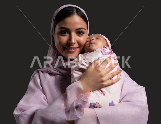 Concern for the comfort and safety of the infant, a close-up portrait of a veiled Saudi Arabian Gulf mother wearing a colorful abaya, holding her daughter and looking at the camera happily, feelings of affection and tenderness between the mother and her children, meeting the children’s needs and taking care of them, black background.