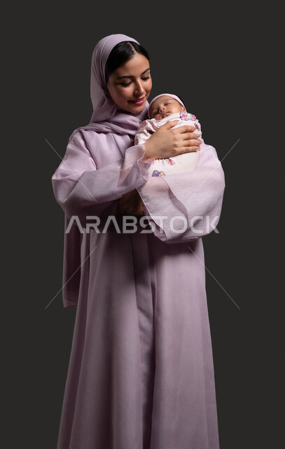إيماءات السعادة والأمان، تعزيز رابط الأمومة بين الأم والطفلة، مفهوم حنان الأمهات و تحمل المسؤولية والعناية بالأطفال، بورتريه لام عربية خليجية سعودية تحتضن ابنتها الرضيعة وتنظر إليها بحب، الشعور بالأمان والاطمئنان، خلفية سوداء.
