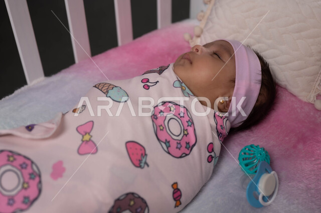 الحفاظ على الدفء والأمان للرضع بتقميطهم بالغطاء، مفهوم البراءة والطفولة، رضيعة عربية خليجية سعودية ملفوفة بغطاء مورد باللون الزهري ومستلقية على ظهرها بهدوء وسعادة ، الحاجة للراحة والاسترخاء، إيماءات السعادة والأمان