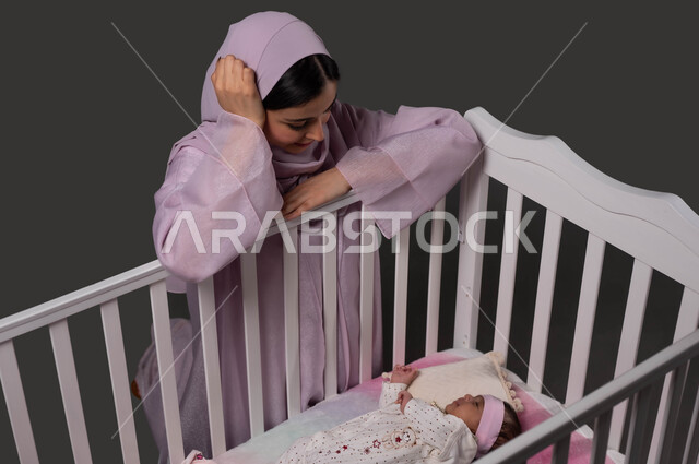 الاستمتاع بقضاء الوقت مع الأبناء، إيماءات الرضا بالسهر على راحة الرضيعة، تقوية رابط الأمومة والبنوة، الشعور بالأمان والاطمئنان، بورتريه لأم عربية خليجية سعودية محجبة تجلس بجانب السرير وتنظر إلى صغيرتها بإيماءات الحب، أجواء الراحة والهدوء، خلفية سوداء