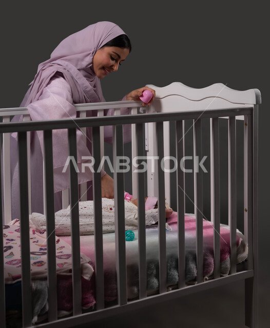 الوجبات الصحية المغذية، استخدام عبوة الرضاعة لشرب الحليب، حنان الأم ورعايتها لأطفالها، بورتريه لإمرأة عربية خليجية سعودية محجبة ترتدي العباءة تعطي رضيعتها الغذاء المفيد، إيماءات الراحة والأمان، مفهوم الرضاعة الصناعية، خلفية سوداء