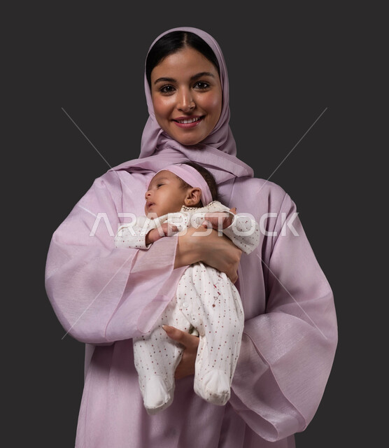 مفهوم حنان الأمهات و تحمل المسؤولية والعناية بالأطفال، تعزيز رابط الأمومة بين الأم وصغيرتها، إيماءات السعادة والسرور، بورتريه مقرب لسيدة عربية خليجية سعودية تنظر إلى الكاميرا تحمل طفلتها الرضيعة بحب، الشعور بالأمان والاطمئنان، خلفية سوداء.