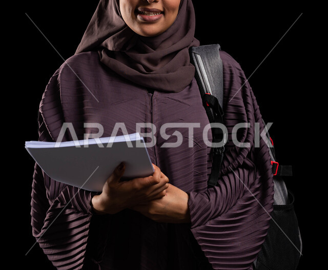 جودة التعليم والتعلم في السعودية, الأكاديميات التعليمية في دول الخليج, الاستعداد للعام الجامعي الجديد, بورتريه مقرب لطالبة جامعية عربية خليجية سعودية مبتسمة محجبة ترتدي حقيبة الظهر تمسك الكتب الجامعية, خلفية سوداء