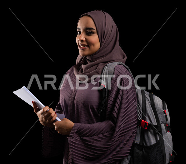 الاستعداد للعام الجامعي الجديد, الكليات والجامعات المتطورة, التعليم والتعلم في السعودية, بورتريه مقرب لطالبة جامعية عربية خليجية سعودية محجبة ترتدي حقيبة الظهر تمسك الكتب الجامعية وتنظر إلى الكاميرا, الأكاديميات التعليمية في دول الخليج, خلفية سوداء