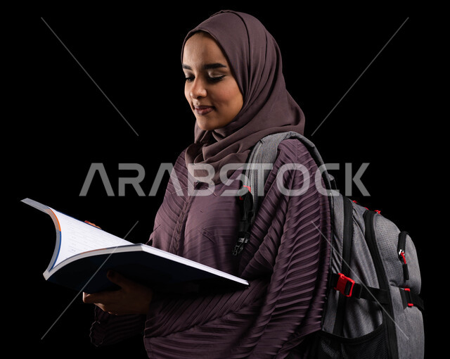 الكليات والجامعات المتطورة, التعليم والتعلم في السعودية, بورتريه مقرب لطالبة جامعية عربية خليجية سعودية محجبة ترتدي حقيبة الظهر تذاكر بالكتاب الجامعي, الأكاديميات التعليمية في دول الخليج, الاستعداد للعام الجامعي الجديد, خلفية سوداء