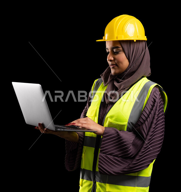 انجاز مهام العمل عبر الجهاز المحمول, بورتريه مقرب لمهندسة عربية خليجية سعودية مبتسمة ترتدي سترة الحماية والخوذة تمسك الابتوب, ادارة المشاريع الهندسية, العمل في القطاع الهندسي, دراسة أساسيات المشروع عبر التطبيقات والتقنيات المتطورة, خلفية سوداء