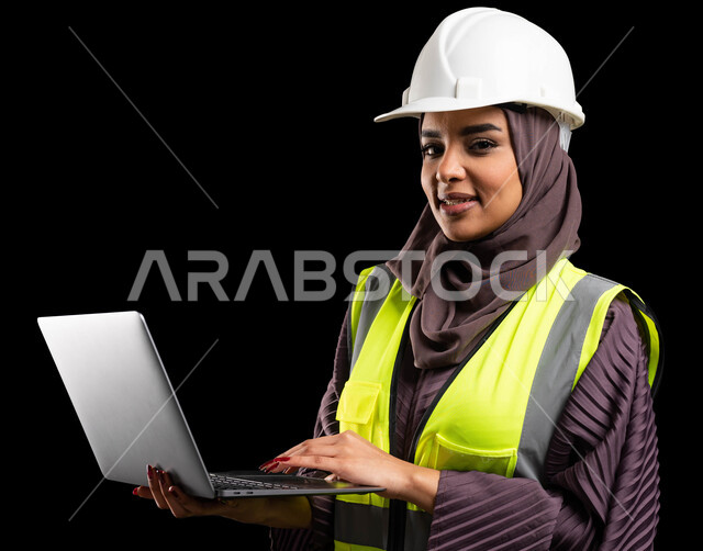 تصاميم ومخططات هندسية, الشغف في مهنة الهندسة, استخدام الأجهزة التقينة الحديثة في المجال الهندسي, بورتريه مقرب لمهندسة عربية خليجية سعودية مبتسمة ترتدي سترة الحماية والخوذة تنظر إلى الكاميرا وتمسك جهاز الحاسوب, مهن ووظائف نسائية, خلفية سوداء