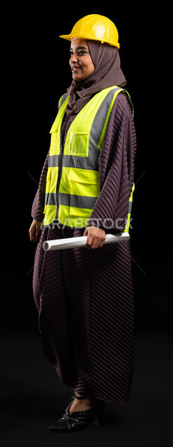 Architectural engineering and construction, the development and progress of Saudi Arabia at the hands of the people of the nation, a portrait of a smiling, veiled Arab Gulf engineer wearing a helmet and a protective vest, holding the reconstruction plan, looking at something, taking care of work affairs, full-length body image, black background