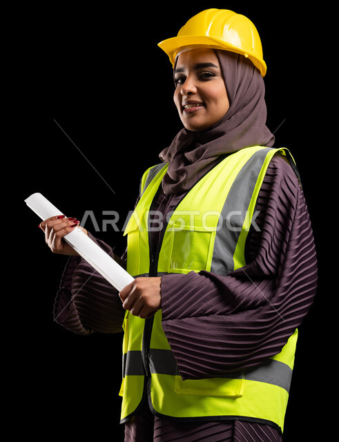 متابعة الأعمال الهندسية, بورتريه مقرب لمهندسة عربية خليجية سعودية مبتسمة ترتدي خوذه الحماية وسترة العمل تقف بإيماءات الثقة والفخر, المخططات الانشائية المعمارية, تطور وتنمية السعودية بمجال الهندسة والبناء على يد أبناء الوطن, خلفية سوداء