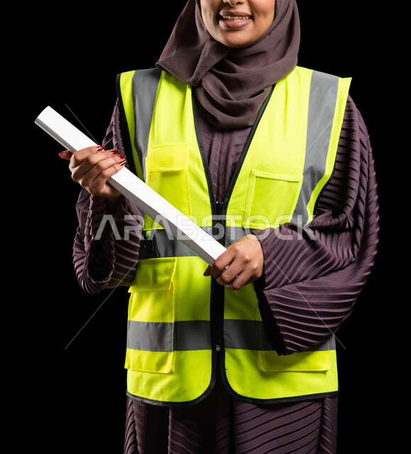 مخططات الإعمار والمشاريع الإنشائية, بورتريه لمهندسة عربية خليجية سعودية مبتسمة ترتدي سترة الحماية تمسك مخطط الاعمار, العمل في القطاع الهندسي, تحقيق حلم النجاح والوصول لمهنة الهندسة, مهن ووظائف نسائية, خلفية سوداء