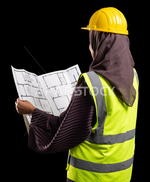 Working in the engineering sector, architectural designs and checking plans, a close-up portrait from the back of a veiled Saudi Arabian Gulf engineer wearing a protection jacket and helmet holding the reconstruction plan, engineering project management, women’s professions and jobs, black background