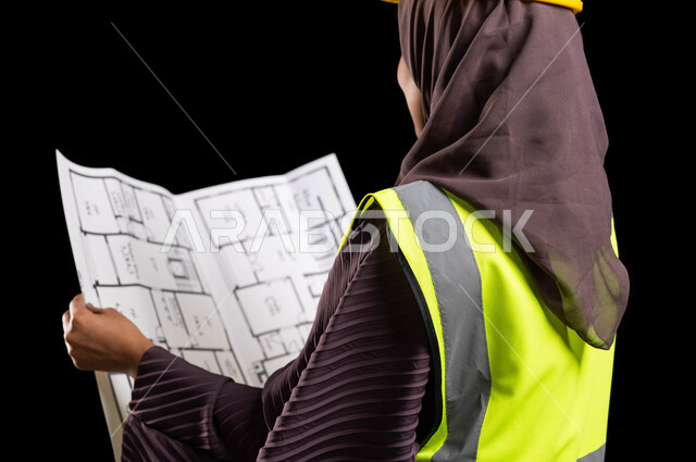تنمية وتطور العمل في المجال الهندسي, التصاميم المعمارية وتدقيق المخططات, بورتريه مقرب من الخلف لمهندسة عربية خليجية سعودية محجبة ترتدي سترة الحماية والخوذة تمسك مخطط الإعمار, إدارة المشاريع الهندسية, مهن ووظائف نسائية, خلفية سوداء