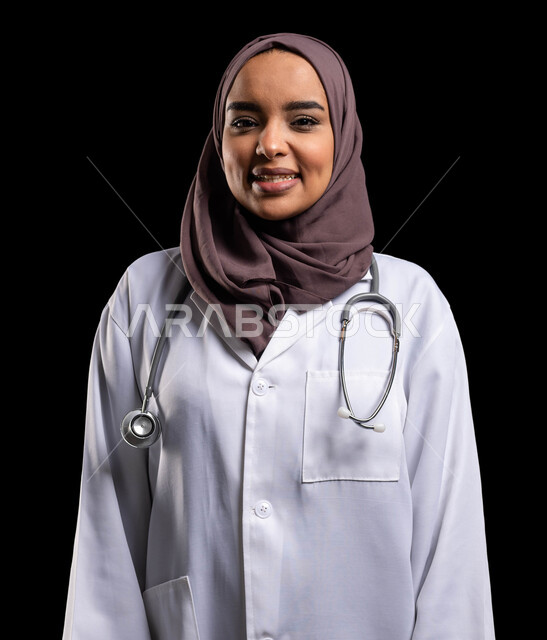 إيماءات الثقة بالنفس والبشاشة, تقديم المساعده الطبية للمرضى, العمل في المراكز الصحية والمستشفيات, بورتريه مقرب لطبيبة عربية خليجية سعودية مبتسمة ترتدي المعطف الطبي الأبيض وسماعة الفحص تنظر إلى الكاميرا, مفهوم الطب والرعاية الصحية, خلفية سوداء