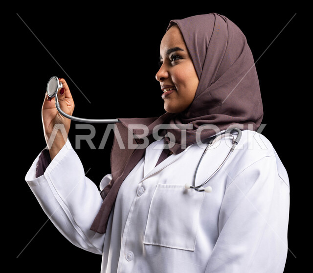 العمل في مجال الرعاية الصحية وتقديم الخدمات الطبية المتميزة، العمل في القطاع الصحي، بورتريه مقرب من الجانب لطبيبة عربية سعودية خليجية محجبة ترتدي المعطف الطبي وتحمل بيدها سماعة الطبيب لسماع نبضات القلب, تطوير القطاع الصحي في السعودية، خلفية سوداء