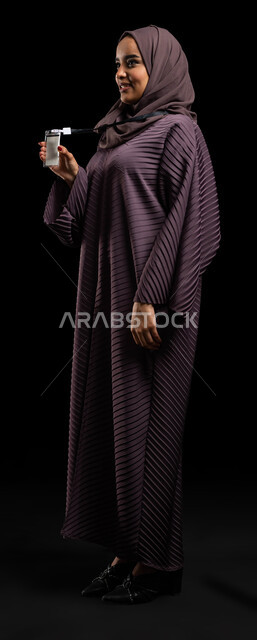 Self-expression, highlighting personal identity, an identification card for students and employees, a portrait of a veiled Saudi Arabian Gulf woman, smiling, holding her ID card in her hand, a blank white card with a black ribbon, self-confidence gestures, a full-length body photo, a black background.