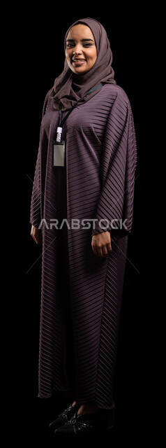 هوية وبطاقه تعريفية، بادج شخصي لطالبة جامعية, بورتريه لإمرأه عربيه خليجية سعودية محجبة مبتسمه ترتدي العباءة وتنظر إلى الكاميرا، بطاقة بيضاء فارغه بشريط أسود، ايماءات الثقة بالنفس, الهوية الشخصية والتعبير عن الذات، صورة الجسم بالطول الكامل، خلفية سوداء