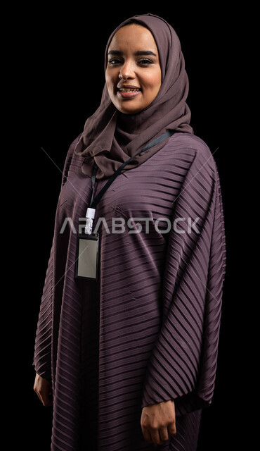 الهوية الشخصية والتعبير عن الذات، بادج شخصي لطالبة جامعية, بورتريه لإمرأه عربيه خليجية سعودية محجبة مبتسمه تضع بطاقة بيضاء فارغه بشريط أسود، بطاقة تعريفية للطلاب والموظفين, ايماءات الثقة بالنفس,  خلفية سوداء